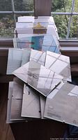 Multiple clear glass photo frames stacked on a surface, showing both front and back sides with metal backing and clips, photographed near a window with natural light.