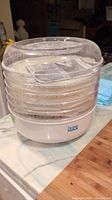 Photo of white electric food dehydrator with six clear stackable trays and a clear lid on a kitchen counter.