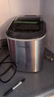 Frigidaire stainless steel portable ice maker on countertop with power cord visible and sharpie marker for size reference.