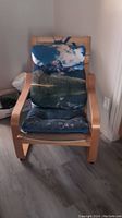 Front view of wooden IKEA Poang chair with scenic cushions showing sky and greenery print.