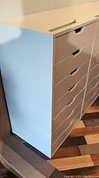 Angle photo showing two white Ikea storage drawer units with 5 drawers each, placed on multicolored wooden floor.