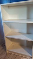 Photo showing the interior of the white small bookshelf with three shelves and minor marks on bottom shelf.