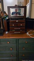Large wooden jewelry box shown with lid open revealing mirror and compartments, side doors open with hooks for hanging jewelry, multiple drawers visible.