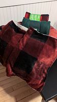 Red and black buffalo plaid queen-sized winter blanket draped over a chair with two additional folded blankets in solid dark green and red-green patterns.