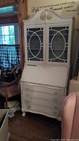 Full view of white painted secretary desk showing closed glass door cabinet and drop-front desk upper closed, curved drawers below with antique style handles.