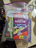 Photo of clear zip lock bag holding multiple kitchen storage products including Hefty slider bags and Reynolds aluminum foil, viewed from top showing product boxes.