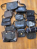 Full overhead view of 13 vintage purses and handbags in black and dark shades, arranged on a wooden floor, showing variety in size and material.