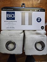 Pack of two The Big One brand room darkening curtain panels, off-white textured fabric, grommet tops visible, packaged and displayed together.