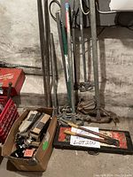Overview of lot showing 7 pipe benders of various sizes standing against wall, red and black Thomas & Betts tool kit case on floor, box of GE circuit breakers, and pry bars.