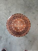 Top view of hand carved round stool with floral patterns and inlay work on wooden surface.