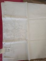 Close-up photo of a hand-stitched white pillowcase with intricate floral embroidery, showing fine stitching and delicate patterns.