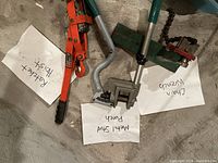 Three main tools laid on floor with handwritten labels: Ratchet Hoist, Metal Stud Punch, Chain Wrench.