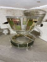 Large glass bowl with metal handles and matching glass plates on metal stand showing green and gold ornate panel design