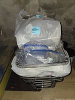 Stack of stainless steel chafing dish frames with wire racks, disposable aluminum foil trays, and chafing fuel in plastic wrapping.