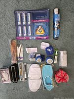 Top-down photo of all personal items arranged neatly on carpet. Includes toothbrush heads pack, electric toothbrush, pedals, slippers, makeup, and hair accessories.