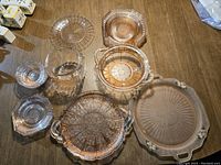 Set includes multiple pieces of pale pink glass dinnerware and serveware on a wooden surface, showing textures and shapes