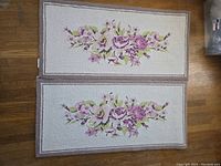 Photo showing one of two wool runners with pale beige background and pink-purple floral design with green leaves, bordered by taupe color.