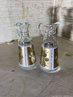 Two small glass pitchers with frosted gold leaf floral patterns and handles placed on a wooden surface.