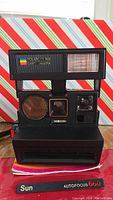 Front view of black Polaroid Sun Autofocus 600 Land Camera showing flash and lens area with rainbow Polaroid logo.