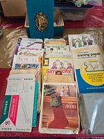 Top down photo showing multiple vintage Simplicity and other brand sewing pattern envelopes and a packet of tracing paper, with a decorative blue box in the background.