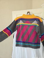 Single colorful geometric patterned sweater shown on hanger, displaying bright stripes and triangular shapes