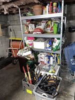 Photo showing metal shelving with various garden fertilizers, weed and grass killers, and gardening supplies including pots and hand tools in crates.