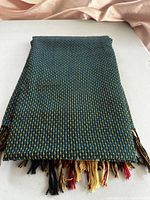 Folded blue and yellow textured woven shawl with multi-colored fringes at the ends.