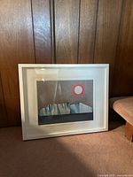 Art print in white IKEA frame approximately 17 x 20 inches leaning against a wood-paneled wall and carpeted floor