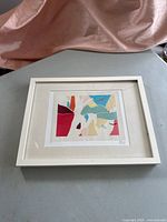 Photo of the framed abstract print showing the entire piece including the white frame and cream matting on a gray tabletop.