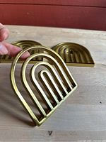 Close-up photo showing one brass arch trivet held by hand to display its shape and size relative to a hand.