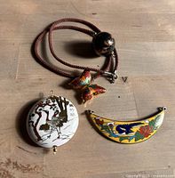 Butterfly necklace and three cloisonné pendants arranged on a wooden surface parallel