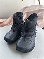 Front view of black Croc winter boots with lace-up closures on a white surface.