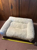 Dog bed showing outer cover with thick bolsters and shaggy fabric, tape measure across showing length
