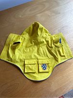 Flat laid yellow dog rain coat with hood, showing front and pockets.