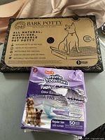 Closed Bark Potty Dog Park in a Box and open pack of Hartz Home Protection dog pads placed on a table.