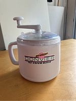 Front and side view of the vintage Donvier ice cream maker showing the handle, hand crank, clear plastic lid, and Donvier logo.