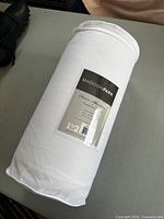 Photo of rolled white Madison Park comforter set in clear packaging on table.