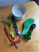 Photo of the Furminator grooming tool, green rubber brush, white pet bowl, and colorful leash extenders on wooden table.