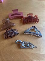 Top view of six hair clips placed on a flat wooden surface, showing variety of shapes and materials.