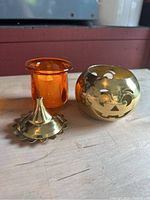 Photo shows brass pumpkin-shaped candle holder separated from its removable lid and amber-orange glass insert, set on wooden surface.