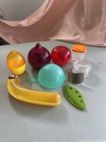 Photo showing colorful kitchen storage containers and tools arranged on a table with a pink drape background.