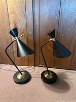 Pair of black and brass MCM style bedside lamps with angled conical shades, circular bases, and USB ports visible.