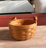Front side view of handwoven Longaberger berry basket with leather handles on wooden surface.