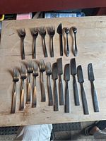 Set of 24 stainless steel flatware pieces on a wooden surface showing knives, forks, and spoons.