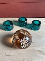 Close-up of three blue cylindrical glass candle holders and single round amber-toned glass paperweight with floral patterns