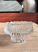 Close-up image of small clear icicle textured glass bowl on wooden surface with red background.