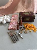 Overview of the lot showing white bud vases, silk embroidery fabric, faux wood birds, metal weights, tassels, spreader knives, heart-shaped bell, pointed stopper, and the wooden box