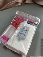 Clear plastic resealable bag filled with various nail tech accessories such as cotton pads, a spray bottle, toe separators, a nail file, and wipes.