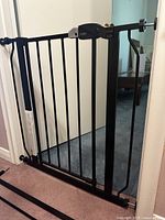 Full view of the black metal expandable pet gate installed in a doorway, showing vertical bars and latch handle.