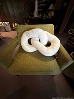 Oversized white bouclé fabric pillow in sculptural interconnected ring shapes on a green chair.